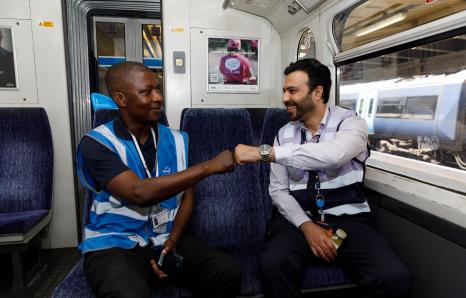 two rail workers sat on a train, fist bumping each other